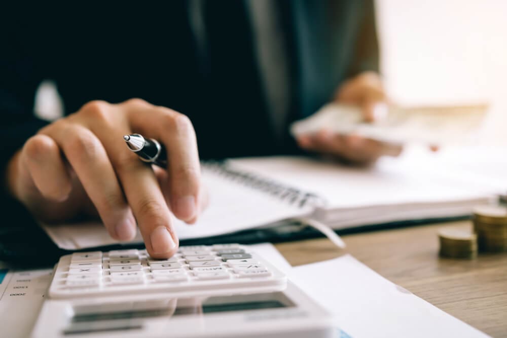 Mãos de uma mulher utilizando calculadora e fazendo contabilidade de suas finanças para declaração do imposto de renda