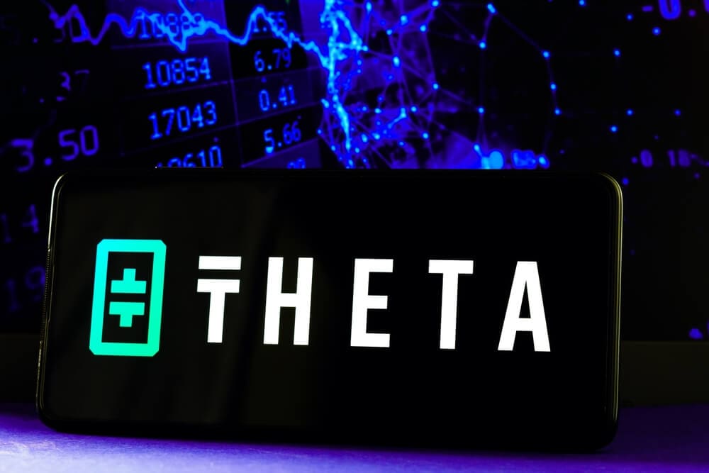 aparelho celular com gráficos financeiros ao fundo reproduzindo em sua tela o logotipo da Theta Network  