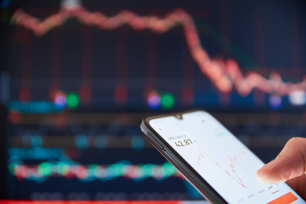 celular na mão de um investidor com sentimento causado pelo fomo analisando o mercado para evitar a perda de oportunidades de investimento